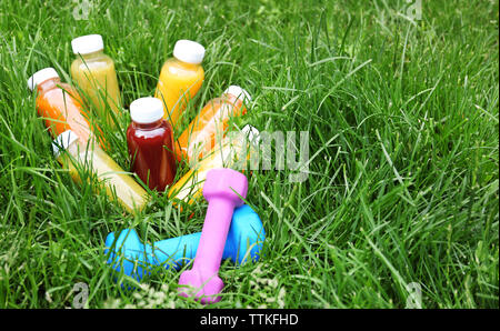 Diät Konzept. Frischer Saft in Glasflaschen und Hanteln auf grünem Gras Stockfoto
