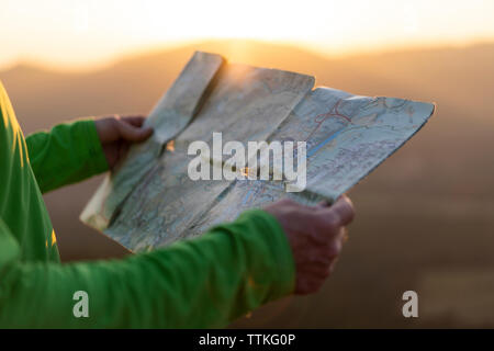 In der Nähe von älteren männlichen Händen hält eine Karte oben auf die Berge bei Sonnenuntergang Stockfoto