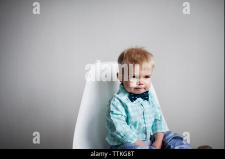 Traurig Baby auf Stuhl gegen weisse Wand zu Hause sitzen Stockfoto