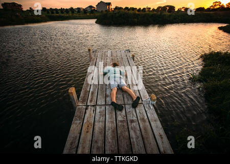 Hohe Betrachtungswinkel der Boy liegend auf der Jetty gegen Himmel bei Sonnenuntergang Stockfoto