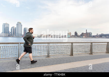 Die volle Länge der übergewichtigen Mann Joggen auf der Brücke am Fluss in der Stadt Stockfoto