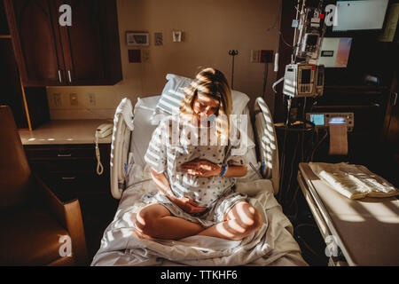 Schwangere Frau berühren Magen beim Sitzen auf dem Bett im Krankenhaus Stockfoto