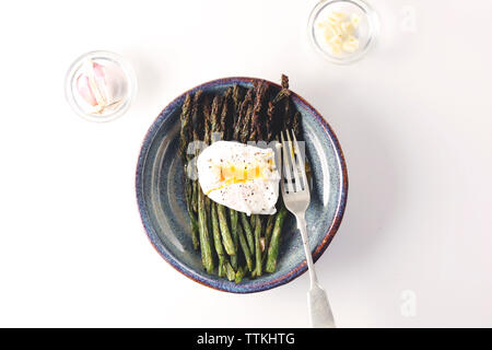 Ansicht von oben von Ei mit Spargel in Platten von Knoblauch und Zwiebeln auf weißem Hintergrund serviert. Stockfoto