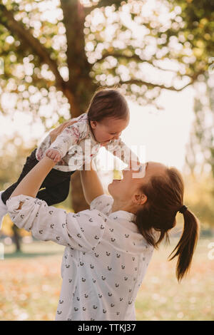 Glückliche Mutter abholen niedlichen Tochter beim Stehen im Park im Herbst Stockfoto