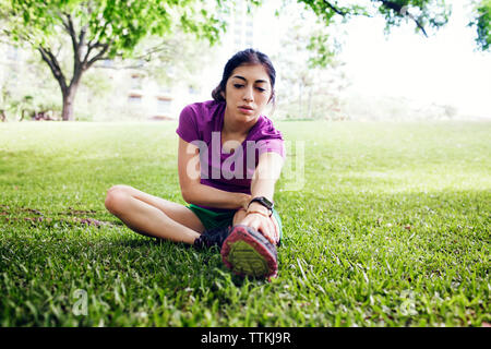 Bestimmt weiblichen Athleten berühren Zehen, während auf dem Rasen im Park sitzen Stockfoto