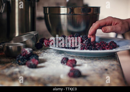 Zugeschnittenes Bild der Frau Hand in Teller mit frischen Brombeeren in Küche Stockfoto