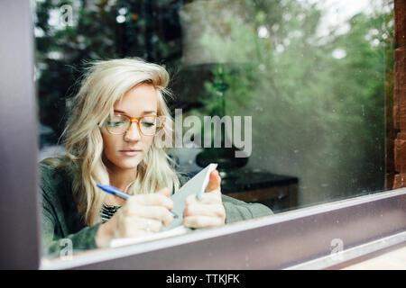 Frau schreiben Tagebuch durch das Fenster gesehen Stockfoto