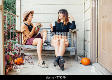 Freundliche weibliche Freunde Drinks während auf holzbank auf der Veranda sitzen Stockfoto