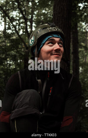 Eine junge lächelnde Kerl sitzt im Wald mit einem Helm auf dem Kopf und Stockfoto