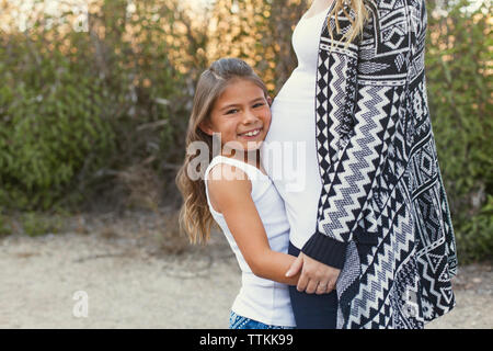 Portrait von glücklichen Mädchen umarmt schwangere Mutter auf dem Feld Stockfoto