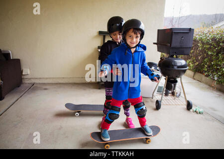 Mädchen Unterstützung Junge, stehend auf Skateboard im Hof Stockfoto