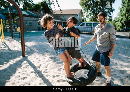 Vater auf der Suche nach Spielende Kinder auf Reifen schwingen im Hinterhof Stockfoto