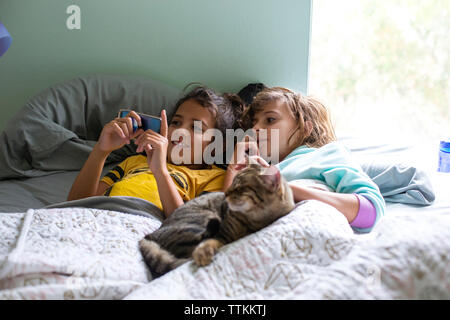 Schwestern auf der Suche nach Smart Phone beim Lügen mit cat auf dem Bett Stockfoto