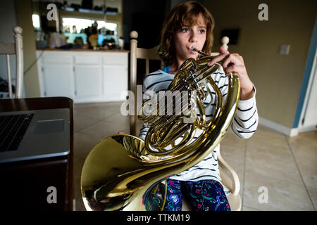 Mädchen spielen Horn während auf Stuhl zu Hause sitzen Stockfoto