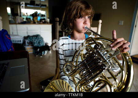 Mädchen üben Horn während auf Stuhl zu Hause sitzen Stockfoto