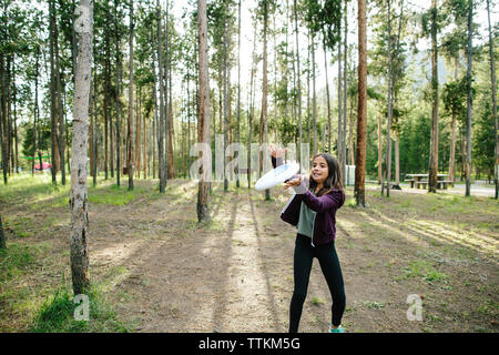 Mädchen fangen Kunststoffscheibe beim Stehen gegen Bäume im Wald Stockfoto