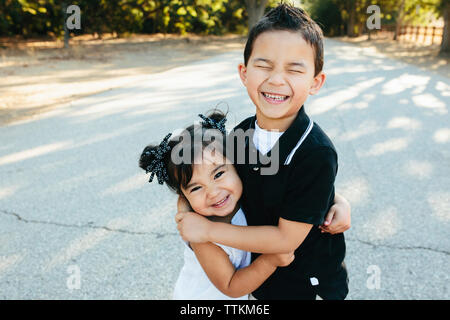 Portrait von Happy Schwester umarmen Bruder beim Stehen auf der Straße im Park Stockfoto