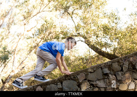 Junge klettert auf eine Mauer aus Stein Stockfoto