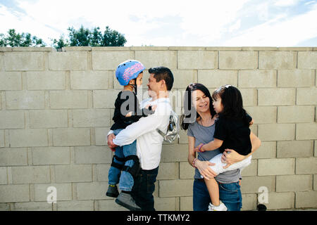 Vater und Mutter halten und bewundern Sie ihre zwei Kinder an einer Wand Stockfoto