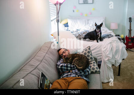 Man schläft auf der Couch mit Katze und Hund auf dem Bett sitzt Stockfoto