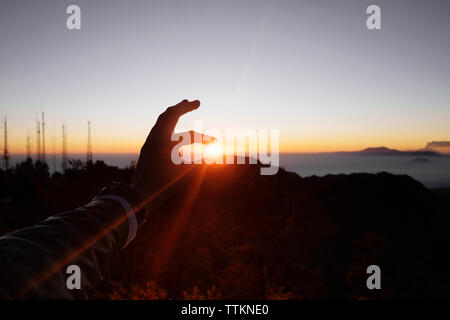 Optische Illusion einer Hand, die Sonne gegen Himmel bei Sonnenuntergang