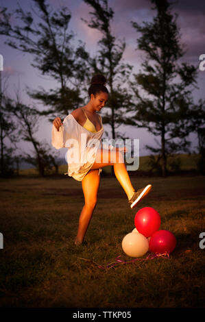 Seitenansicht des happy Teenager platzen Ballons auf Feld in der Dämmerung Stockfoto