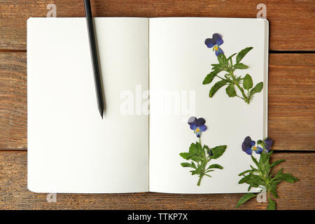 Schöne getrocknete Blüten im Notebook auf hölzernen Hintergrund Stockfoto
