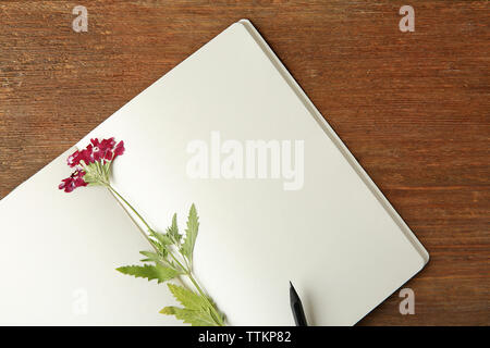Schöne getrocknete Blüten im Notebook auf hölzernen Hintergrund Stockfoto