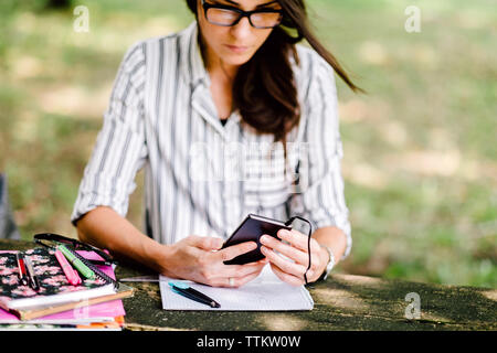 Frau mit Büchern auf dem Tisch mittels Smart Phone im Wald sitzen Stockfoto