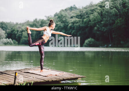 Frau Yoga beim Stehen auf Pier über den See im Wald Stockfoto