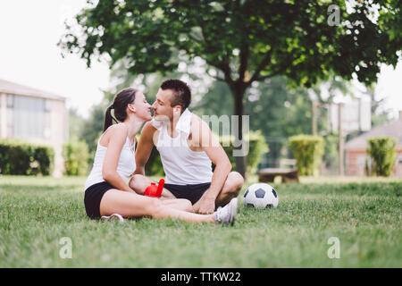 Junges Paar küssen beim Sitzen auf Fußball im Park Stockfoto