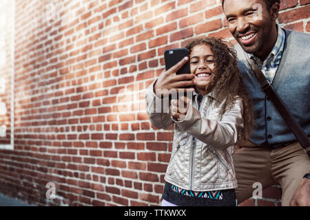 Tochter von selfie mit Vater durch Smart Phone gegen Mauer Stockfoto