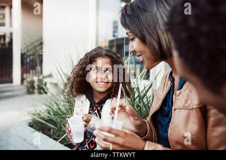 Mutter und Tochter genießen Trinken beim Sitzen auf Stützmauer Stockfoto