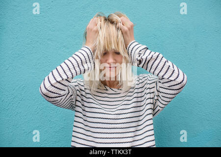 Frustrierte junge Frau Haar ziehen gegen blaue Wand Stockfoto