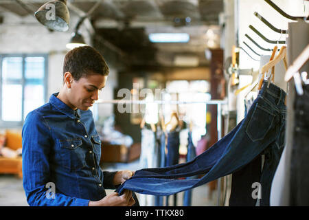 Lächelnd Fashion Designer Kontrolle jeans hängen an Rack in Werkstatt Stockfoto