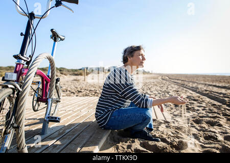 Nachdenkliche Frau spielen mit Sand, während mit dem Fahrrad am Strand sitzen Stockfoto