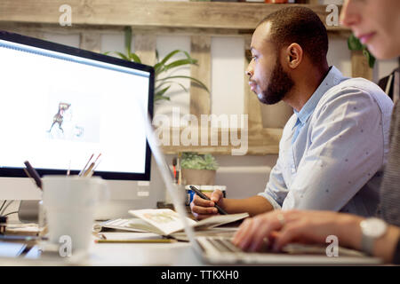 Seitenansicht von Illustrator, Malerei auf Computer mit Kollegen mit Laptop auf dem Schreibtisch in der kreativen Büro Stockfoto