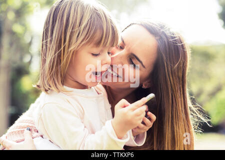 Glückliche Mutter mit Tochter mittels Smart Phone in Park Stockfoto