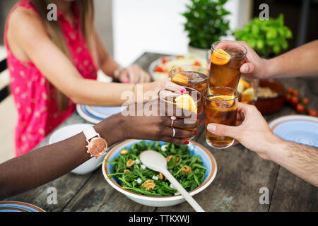 Zugeschnittenes Bild von Freunden toasten Eistee Gläsern am Tisch im Freien Stockfoto