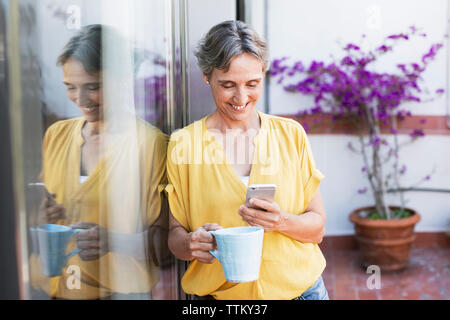 Gerne reife Frau mit smart phone halten Kaffeetasse auf der Veranda Stockfoto