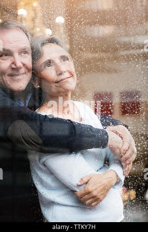 Liebevolle senior Paar durch nasses Fenster Stockfoto