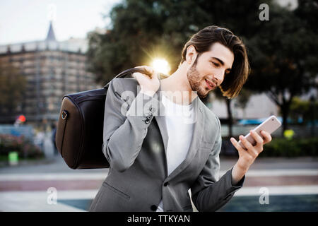 Geschäftsmann, der seine Tasche trägt, während er das Mobiltelefon benutzt Stockfoto