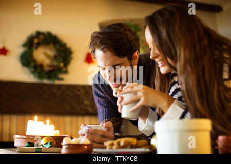 Ein lächelndes Paar, das an weihnachten Kaffee am Tisch trinkt Stockfoto