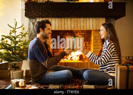 Glückliches Paar, das zu Hause ein weihnachtsgeschenk am Kamin hält Stockfoto