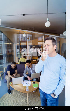 Geschäftsmann, der auf dem Mobiltelefon spricht, während Kollegen im Hintergrund diskutieren Stockfoto