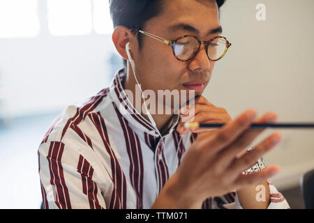 Geschäftsmann, der während der Arbeit im Büro Kopfhörer verwendet Stockfoto