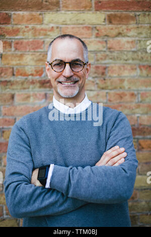 Portrait von zuversichtlich Mann mit verschränkten Armen stehend gegen Mauer Stockfoto