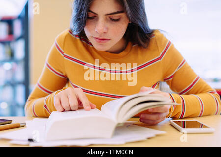 Frau mit Buch beim Sitzen am Tisch in der Bibliothek Stockfoto