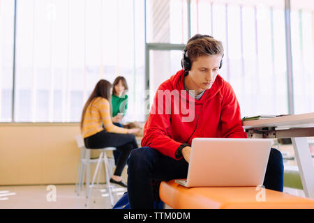Mit Laptop, während weibliche Freunde studieren im Hintergrund bei Bibliothek Mann Stockfoto