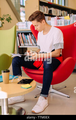 Mann schreiben beim Sitzen auf Stuhl in der Bibliothek Stockfoto